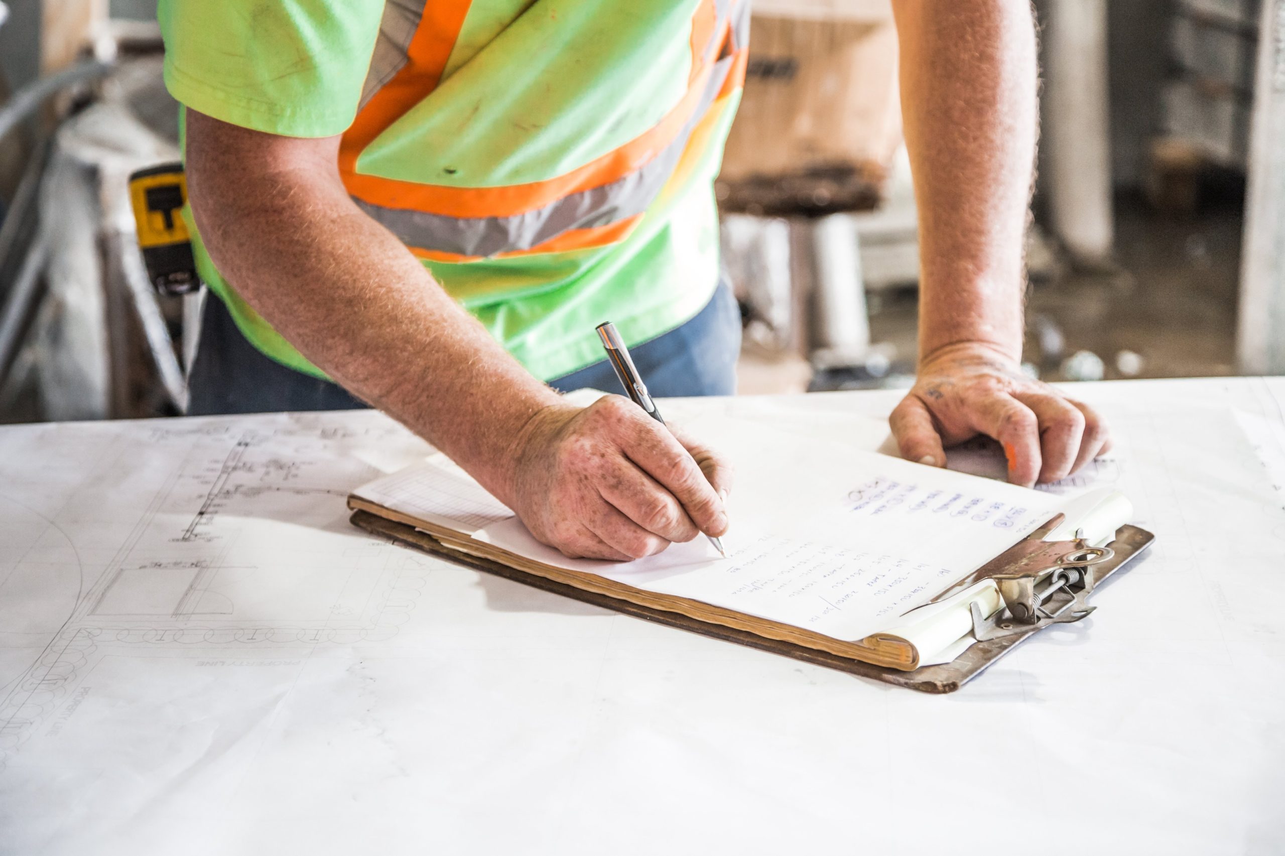 man writing on clipboard wearing safety vest