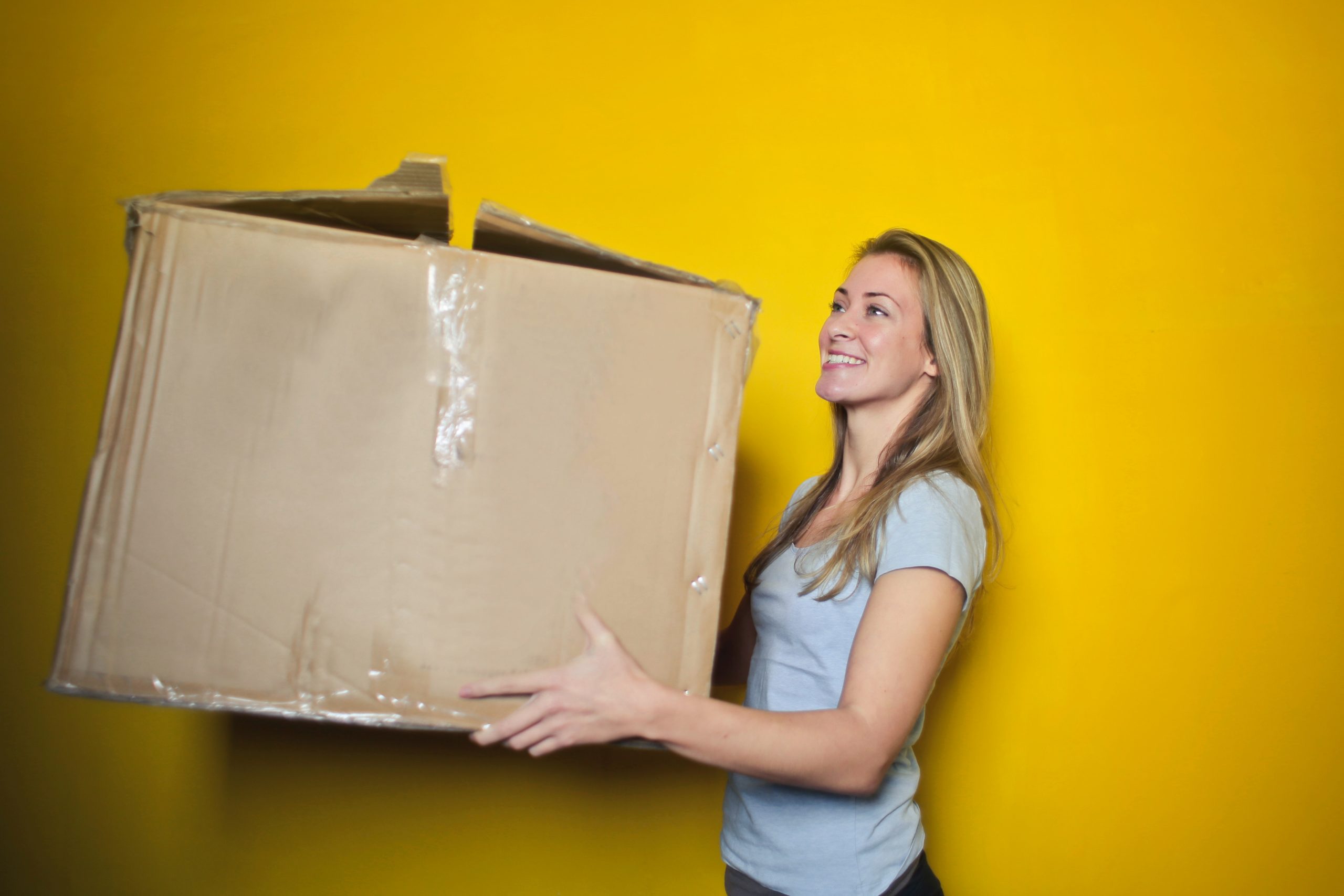 Blonde woman with moving box in front of a gold wall
